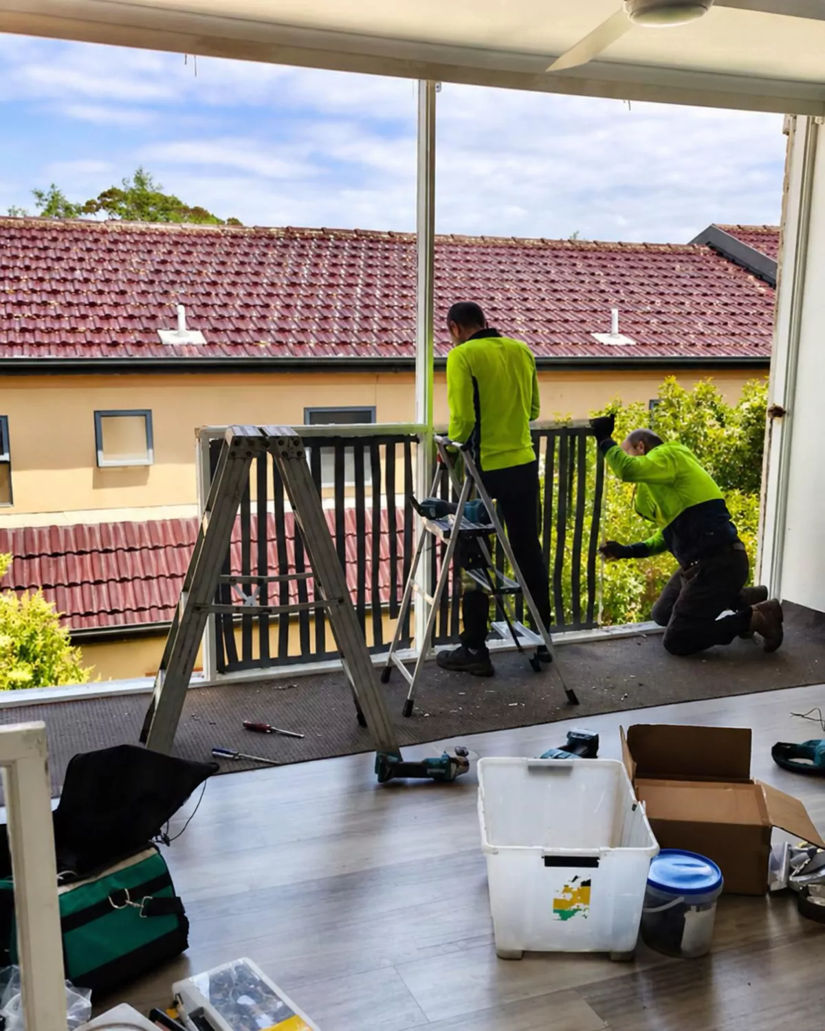 Two Glassy Slide installers fitting aluminium window frames along an upstairs balcony