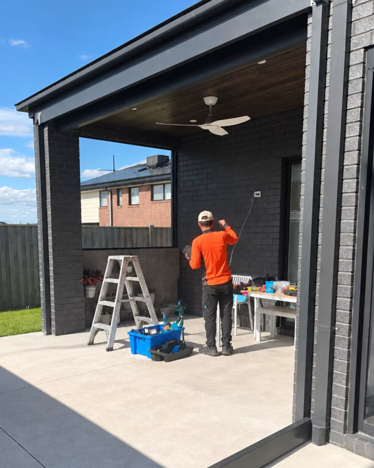 A Glassy Slide installer working under the existing alfresco, beside a dark brick wall and ceiling fan